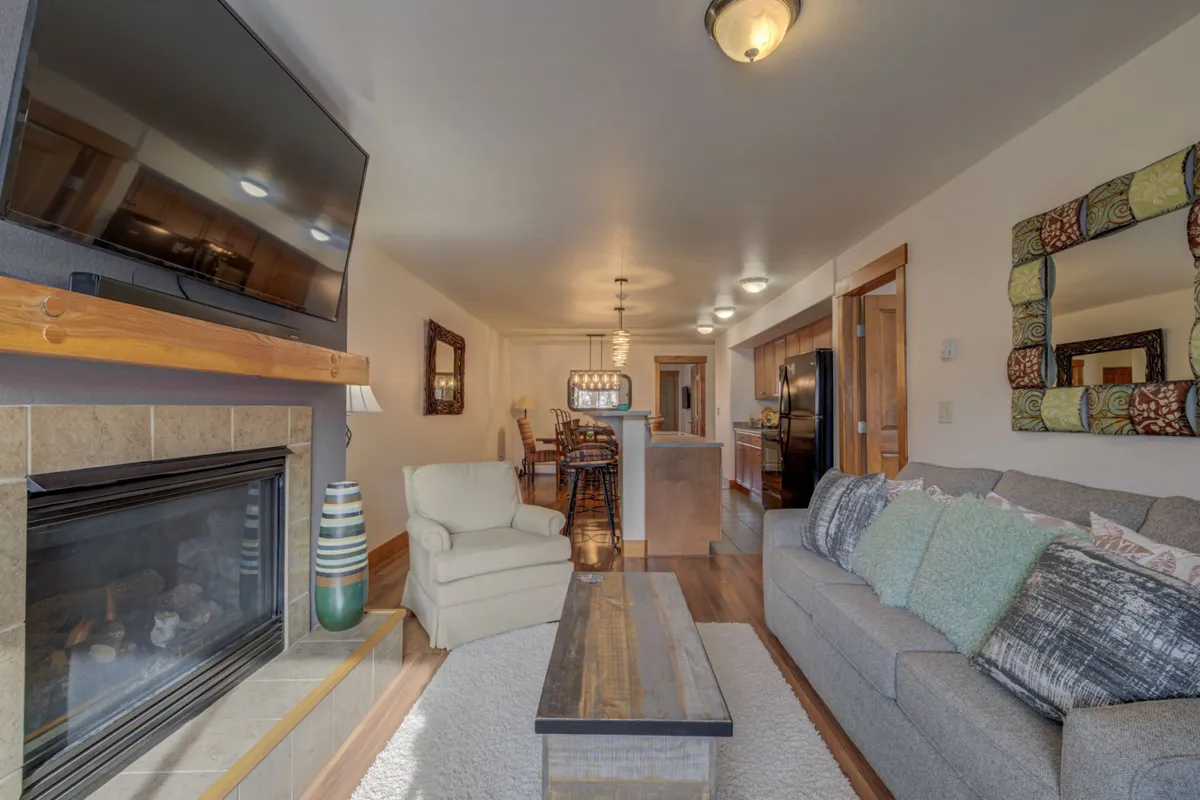 This image features a cozy open-plan living/dining space with a prominent fireplace, sofa, and kitchen island—an ideal setting for après-ski relaxation, socializing, and family dining. The mood is warm and inviting, perfect for unwinding after a day on the slopes.