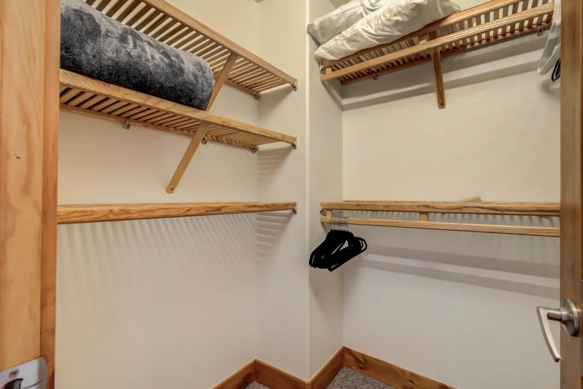 A practical closet with wooden shelving, stacked blankets, and hangers offers a glimpse of the type of hallway closet where a washer and dryer might be found, emphasizing storage and organization for gear.