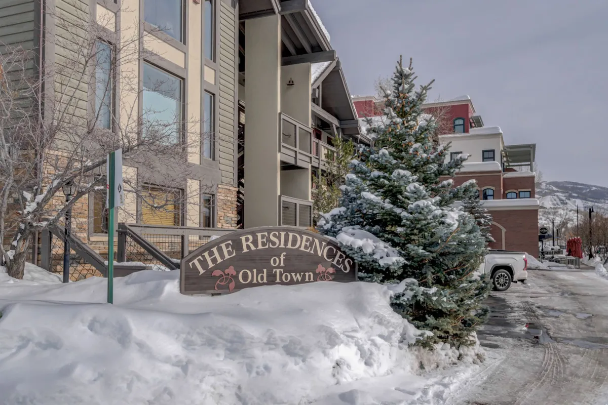 A welcoming exterior shot of 'The Residences of Old Town' sign, flanked by snow-covered trees and the building's facade. The wintry setting highlights the property's inviting atmosphere and its proximity to outdoor fun.