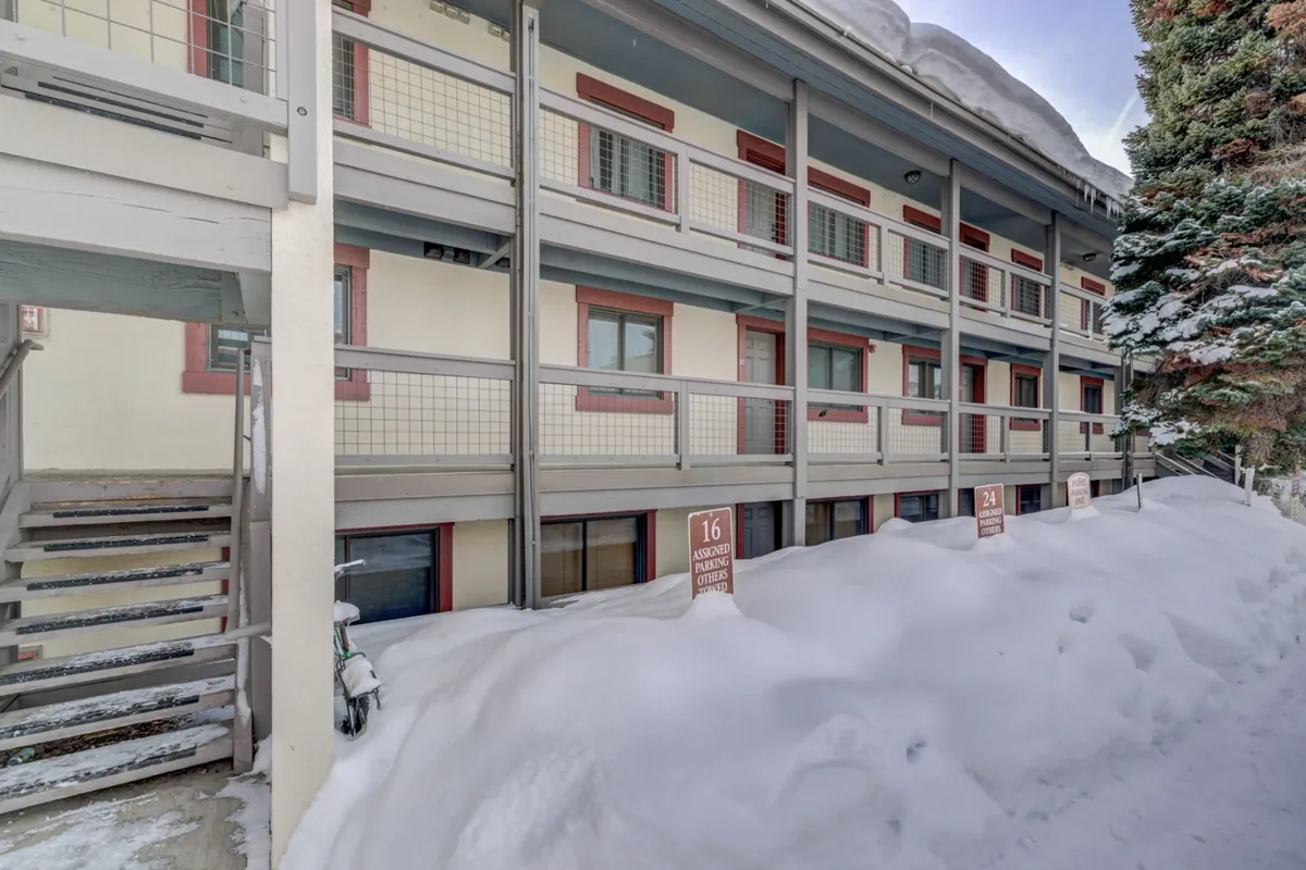 A wintery exterior scene featuring snow-covered ground, balconies overlooking the landscape, and a prominent staircase. The mood is calm and inviting, with hints of winter sports and relaxation. The snow suggests the year-round adventure described, particularly winter activities like snowshoeing and Nordic skiing at nearby Howelsen Hill.