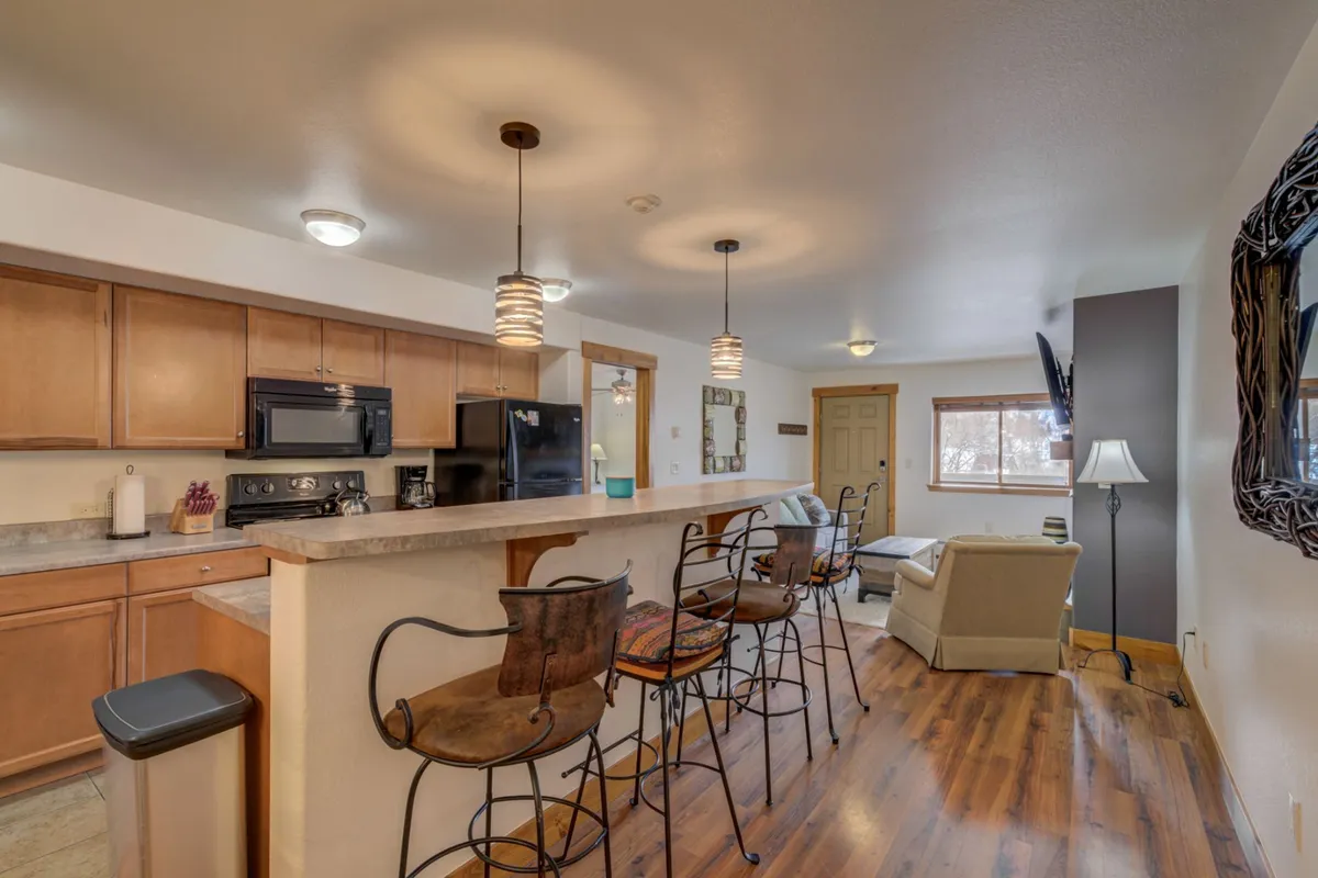 A bright, open kitchen and living area with a kitchen island and bar stools, accented with decorative wall art. The space merges cooking, relaxing, and socializing, and offers a glimpse of the transition between home comforts and group gatherings.